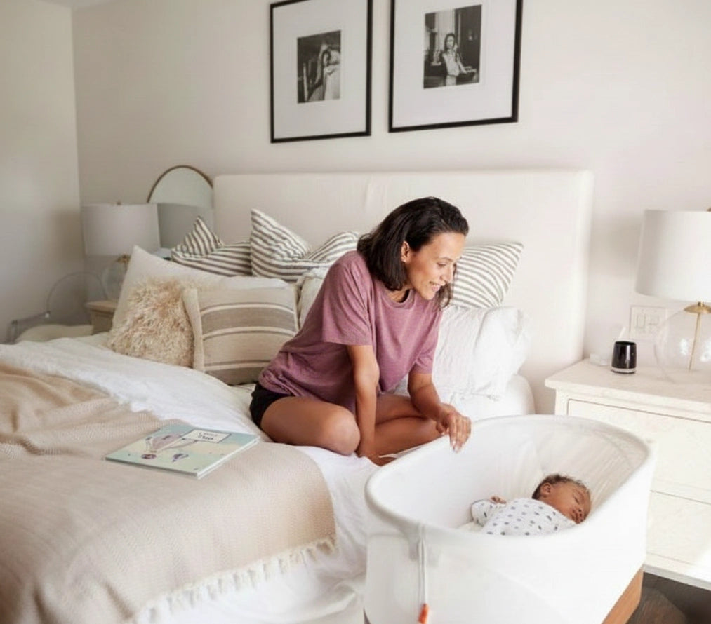 Maman qui regarde son nouveau-né dans son berceau, l'album montgolfière Antoinette & Louis est posé sur le lit à côté d'elle